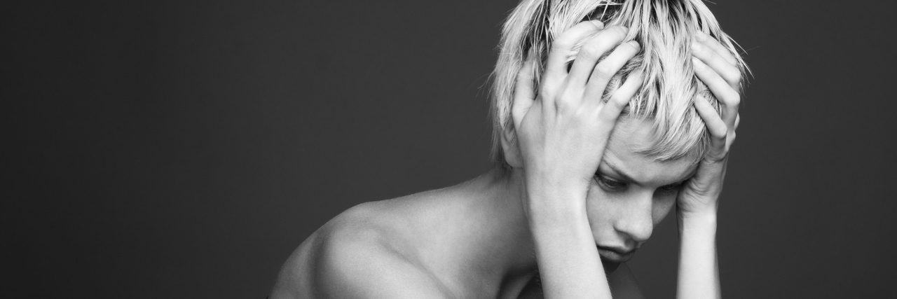 A black and white image of a woman with her hands to her head, looking upset.