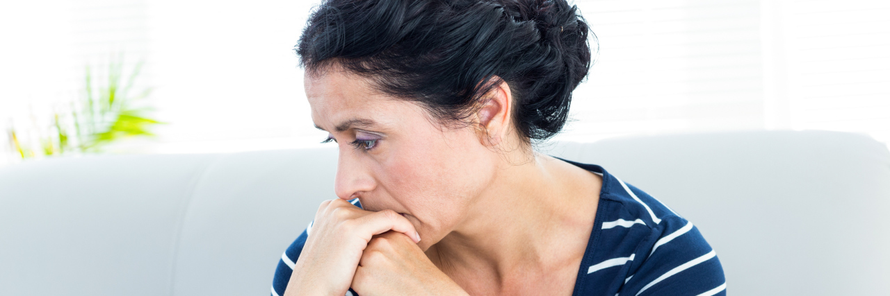 The Fine Line Between Chronic Illness and Depression A picture of a woman sitting on a couch, looking distressed.