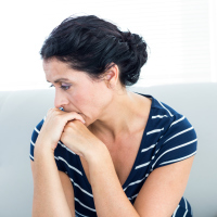 A picture of a woman sitting on a couch, looking distressed.