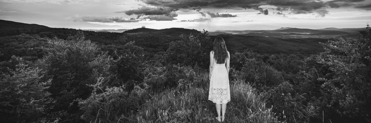 What It's Like Being Asked 'How Are You?' A black and white image of a woman standing in a grassy field with fields above.