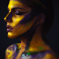 A picture of a woman with paint on her face and body, mostly yellows and some purple.