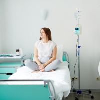 Young woman sitting on bed in hospital ward