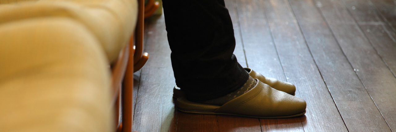 A picture of someone's feet on a wooden floor in a waiting room.