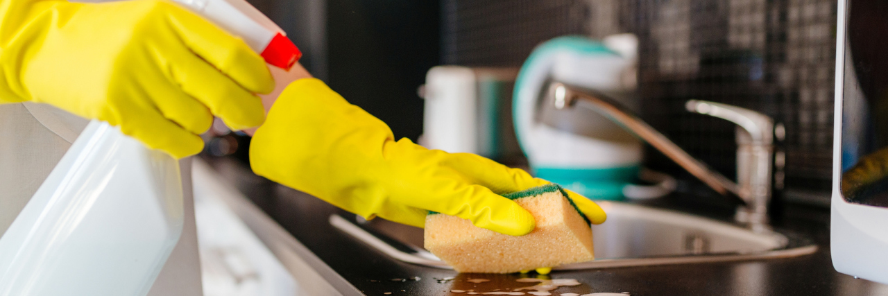 A woman cleaning a kitchen counter with a spray bottle and sponge.