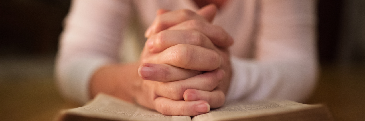 Why Christians Need to Stop Stigmatizing Mental Illness Unrecognizable woman praying with hands clasped together on her Bible. Close up.