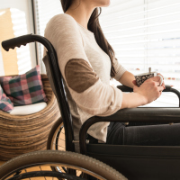 A woman sitting in a wheelchair, holding a cup of tea, while looking out the window.