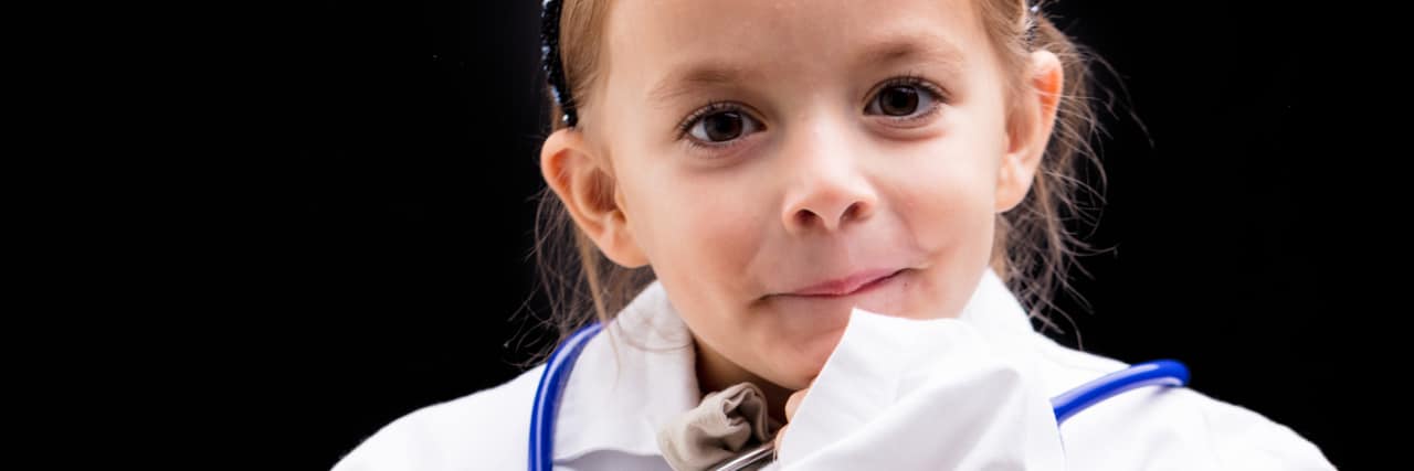 When My Little Sister Wants to Play 'Doctor' A child wearing a white doctor's coat with a stethoscope, and looking curious with her hand to her chin.