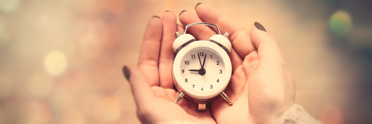A picture of a woman's hands holding a small, white clock.