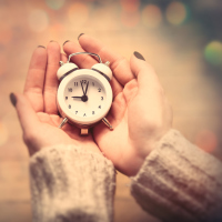 A picture of a woman's hands holding a small, white clock.