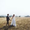 A picture of a bride and groom walking in a field.