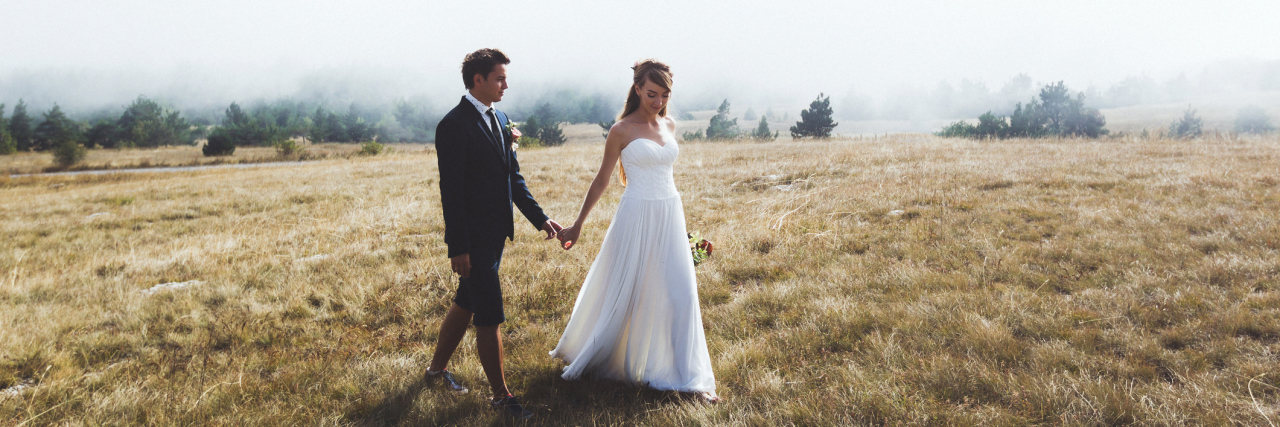 To My New Husband, From Your Chronically Ill Wife A picture of a bride and groom walking in a field.