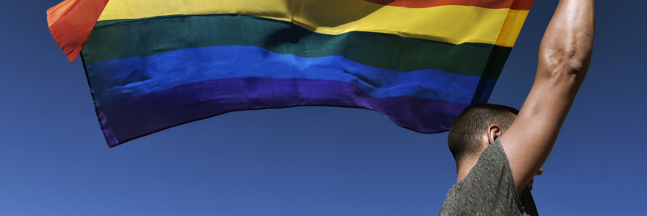 A person holding up a rainbow flag against the blue sky