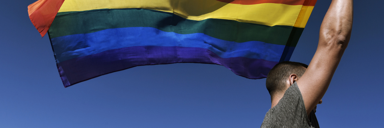 Letter for Anyone Struggling With Depression During Pride Month A person holding up a rainbow flag against the blue sky