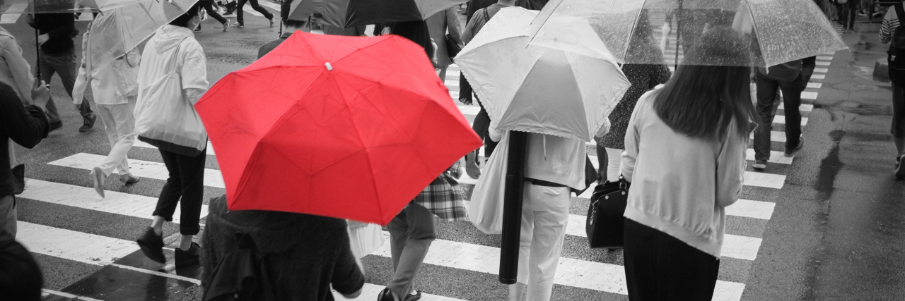 A red umbrella in a crowd of people crossing the street.