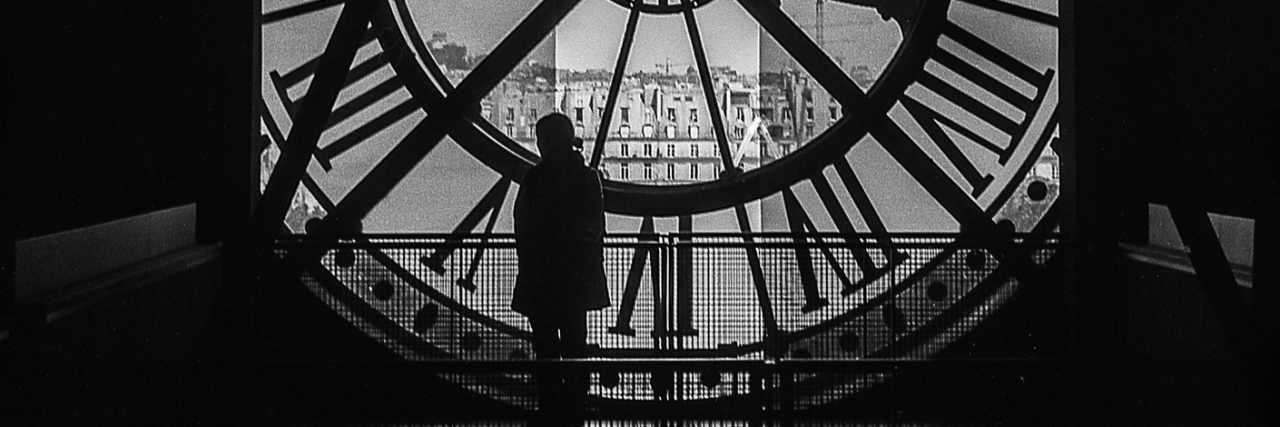 A woman standing inside a tower, in front of a giant clock.