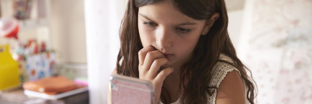 A picture of a worried looking little girl, staring at a phone while biting her nails.