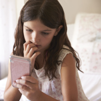 A picture of a worried looking little girl, staring at a phone while biting her nails.