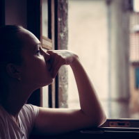 Pensive thoughtful young woman lost in thoughts dreaming and looking into opened window in vintage style with dramatic mood