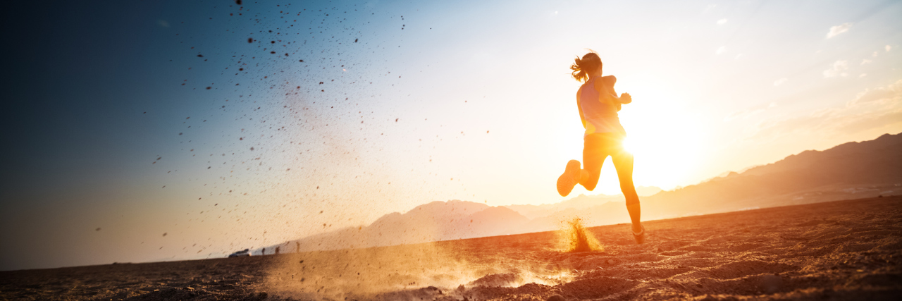 A picture of a woman running in a sandy desert as the sun is setting.