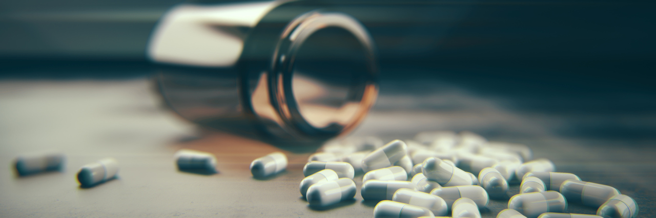 Fallen bottle and scattered pills on concrete background.