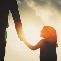 Silhouette of little girl holding father's hand.