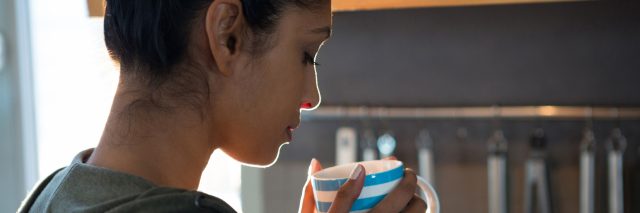 A young woman in her kitchen drinking a cup of tea.