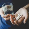 woman holding pills in hand and glass of water