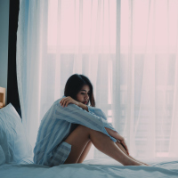 A woman sitting on a bed looking sad and lonely