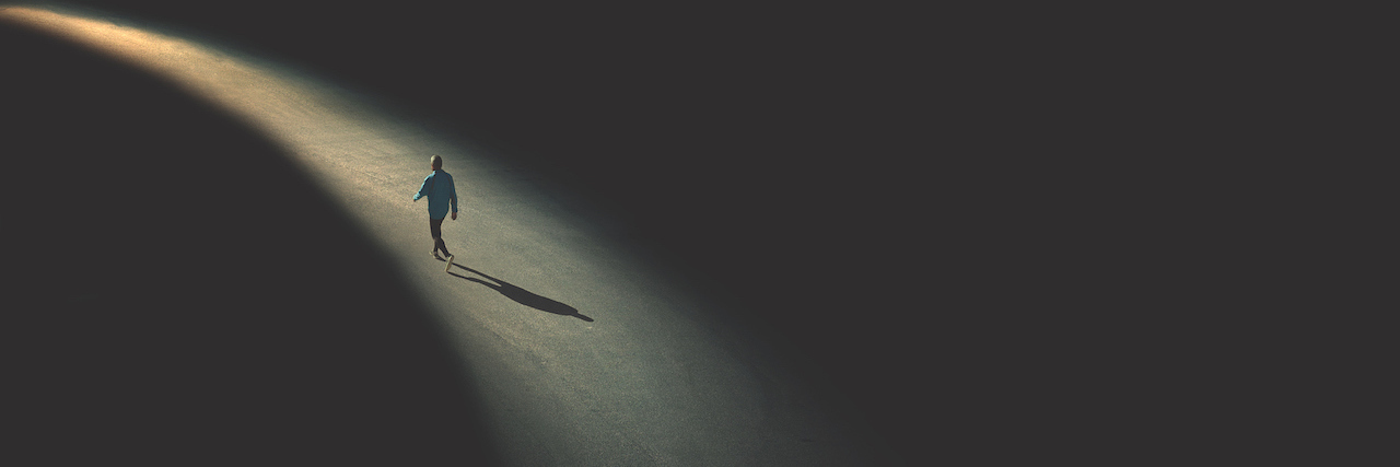 Loneliness Isn't an 'Epidemic' That Needs to Be Solved A man walking in the dark, following a path that is lit. He is alone.