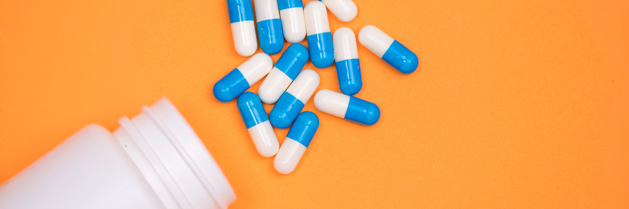 antibiotic medical drug capsule falling from bottle on orange background