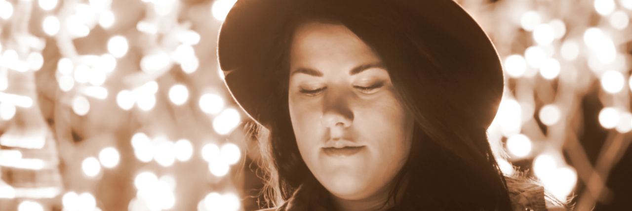 Let's Address the Assumptions People Are Making About My Weight A woman looking at her phone outside, with beautiful lights hanging behind her.