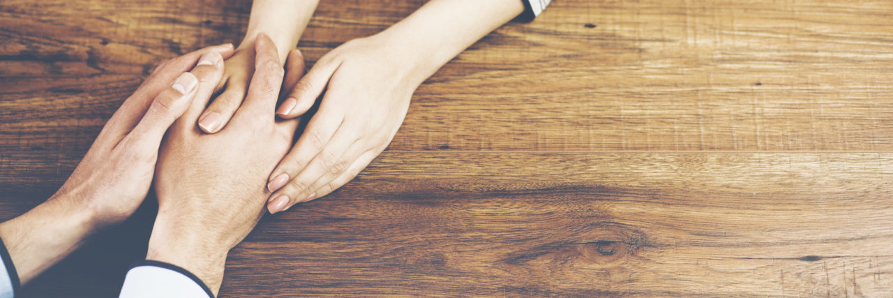 Close up on a man and a woman holding hands at a wooden table