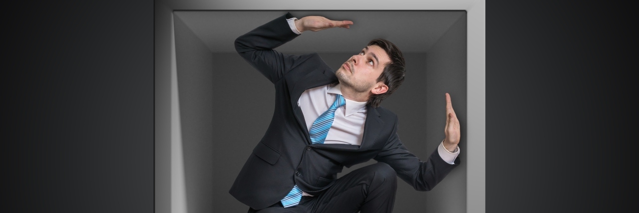 Businessman trapped inside uncomfortable small box.