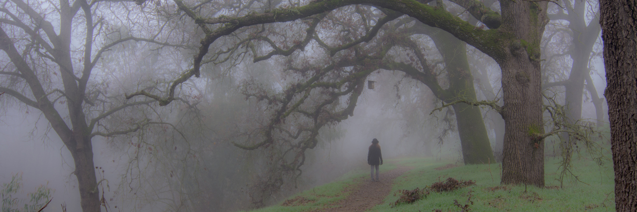 When Self-Doubt Became a Symptom of My Chronic Illness A woman walking into a layer of fog in the woods.
