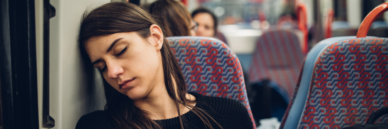 What Traveling Is Like When You Live With Multiple Chronic Illnesses A tired woman sitting on a train, her head resting on the wall by her seat.