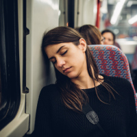 A tired woman sitting on a train, her head resting on the wall by her seat.