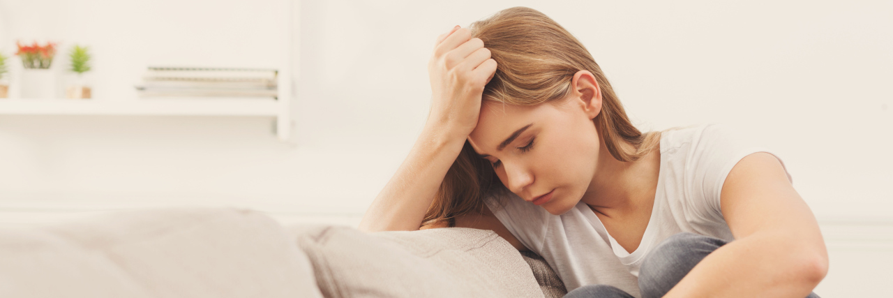 I Am Not Defined by My Headaches A woman sitting on a couch with her hand up to her head, looking like she's in pain.