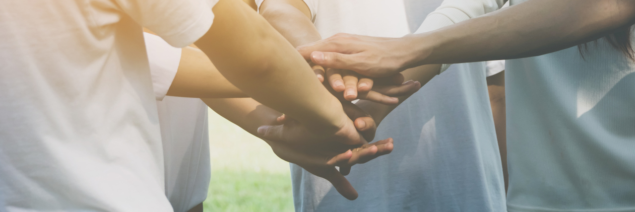 Myasthenia Gravis Awareness Month What It Means to Be Aware people stacking their hands on top of one another outside