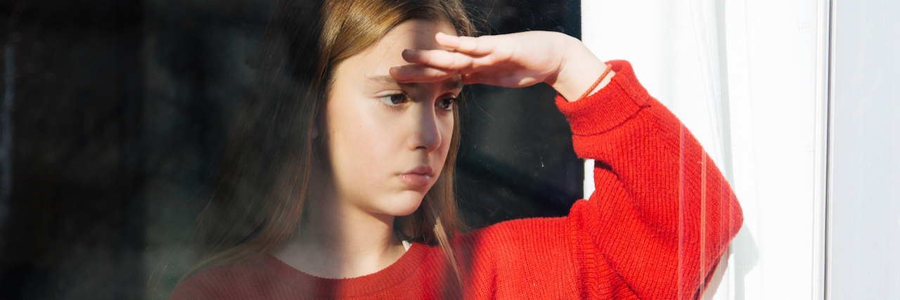 A young girl wearing a big sweater looking out a window