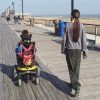 Mother walking side by side with son who is using motorized wheelchair as they go down a wooden walkway.