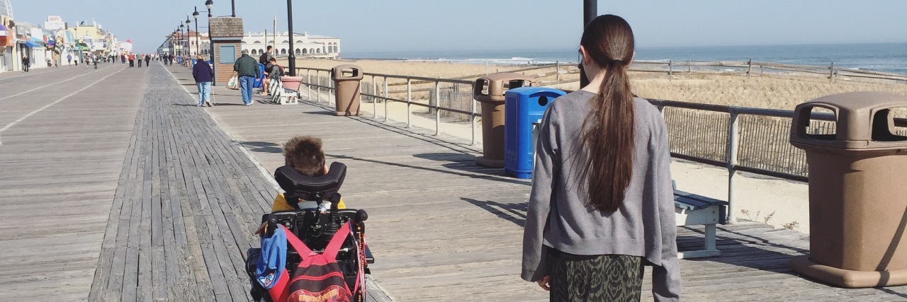 I Am Not Exceptional for Parenting a Child With a Disability Mother walking side by side with son who is using motorized wheelchair as they go down a wooden walkway.