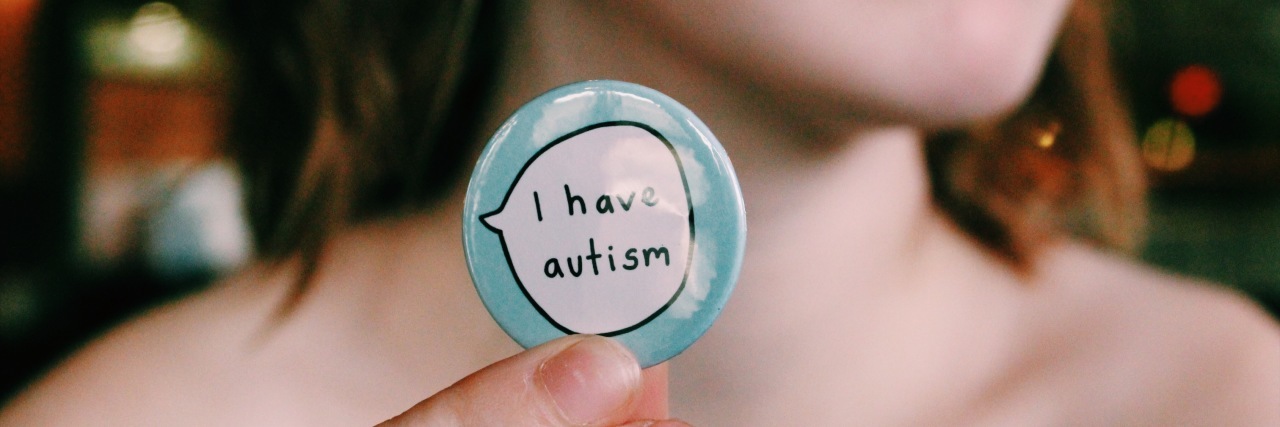 Young woman holding a button that says "I have autism."