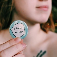 Young woman holding a button that says "I have autism."