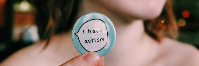 Young woman holding a button that says "I have autism."