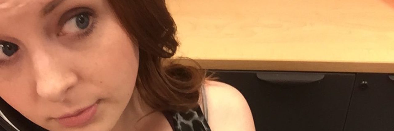 Why I'm Proud of My Poker Face During a Fibromyalgia Flare A picture of the writer on her office phone, with a heating pad on her stomach.