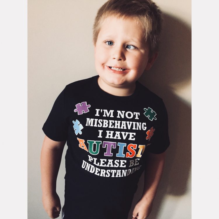 Boy smiling at camera wearing shirt that reads: I am not misbehaving, I have autism please understand 
