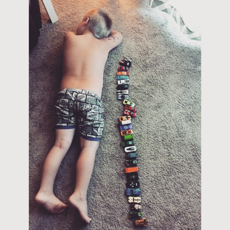 Boy with autism sleeping on floor next to his toy cars lined up