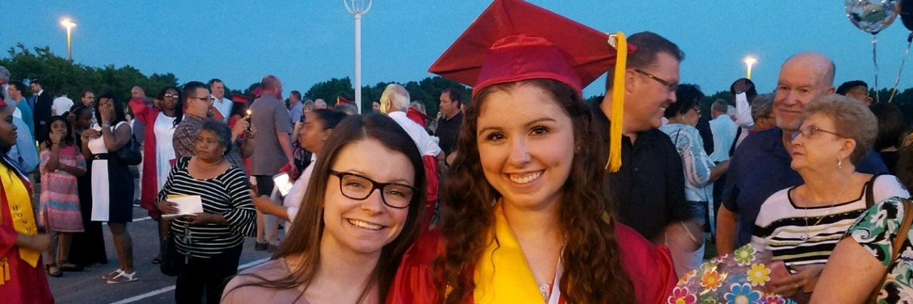 A picture of the writer wearing a red graduation gown, standing next to her friend.