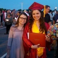 A picture of the writer wearing a red graduation gown, standing next to her friend.