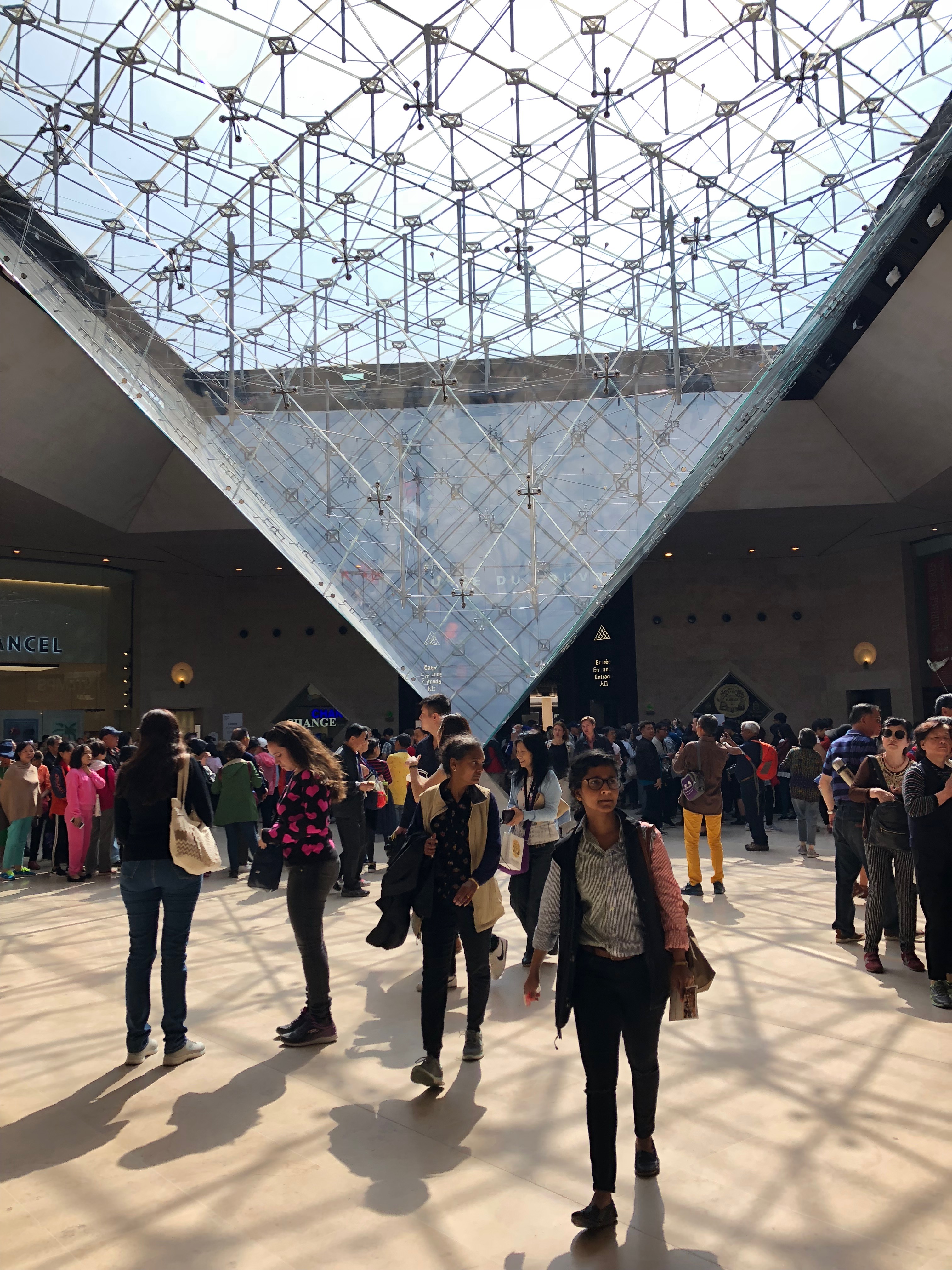 A crowd forms around the interior of the Louvre's iconic pyramid. 